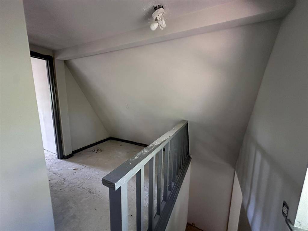 This image shows a small, unfinished room with sloped ceilings, a simple railing, and bare floors. It appears to be a loft or attic space in need of renovation.