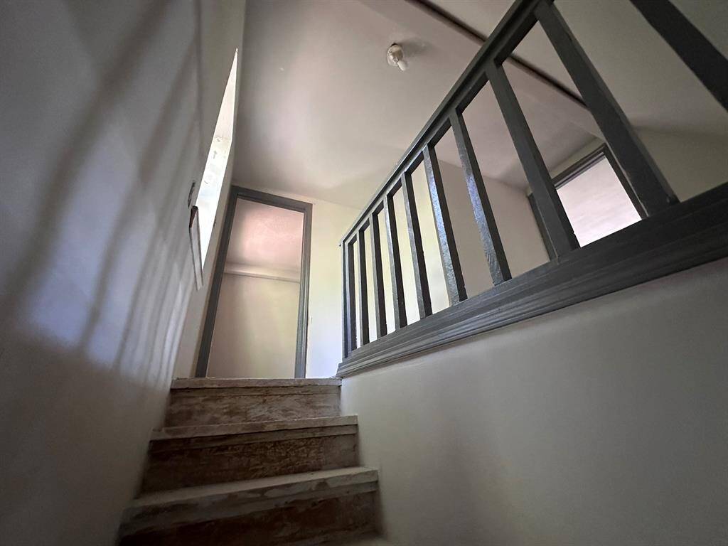 This photo shows a narrow staircase with unfinished wooden steps leading to an upper floor. It features a simple railing and a small window, providing natural light.