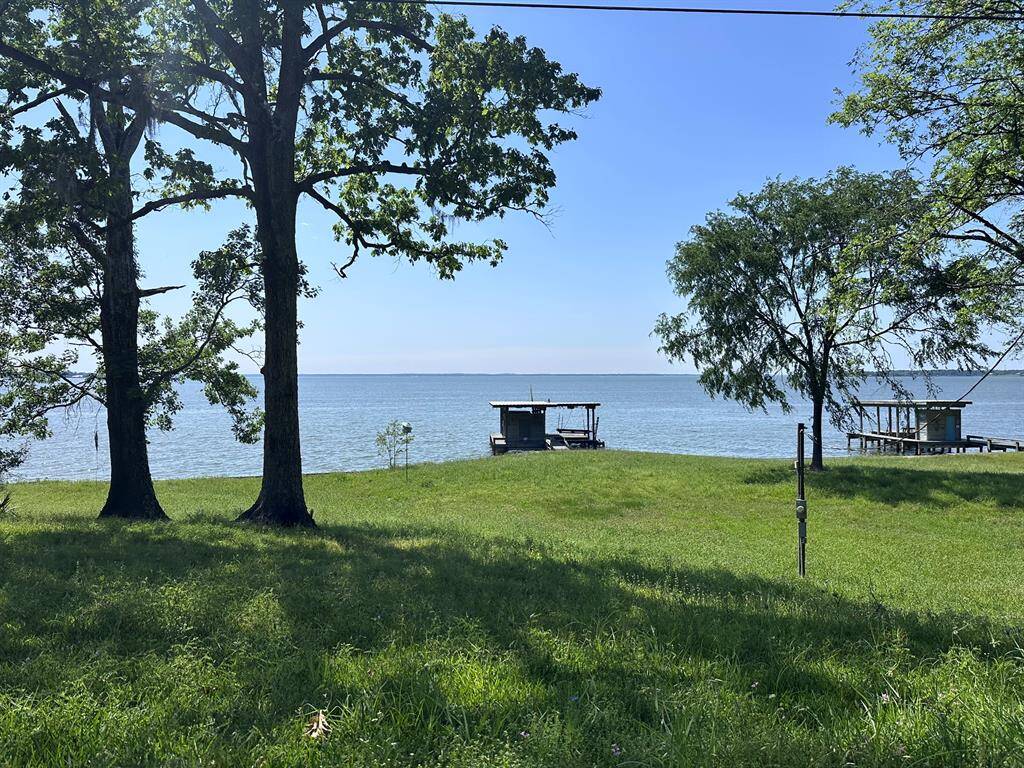 This serene lakeside property features a spacious grassy area leading to the water's edge, with picturesque views framed by mature trees and a wooden dock. Ideal for relaxation and enjoying nature.