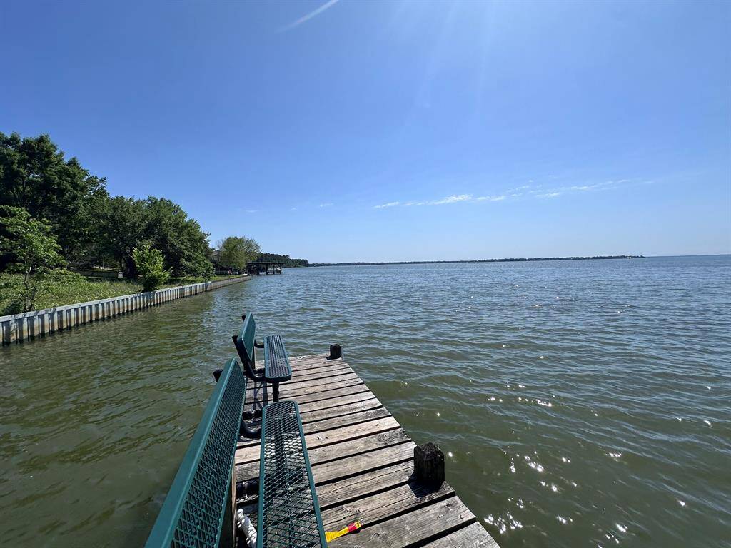 This photo features a serene lakeside view with a wooden dock extending into the water, perfect for relaxation. The shoreline is lined with trees, offering a peaceful and natural setting. Ideal for those seeking a tranquil waterfront property.