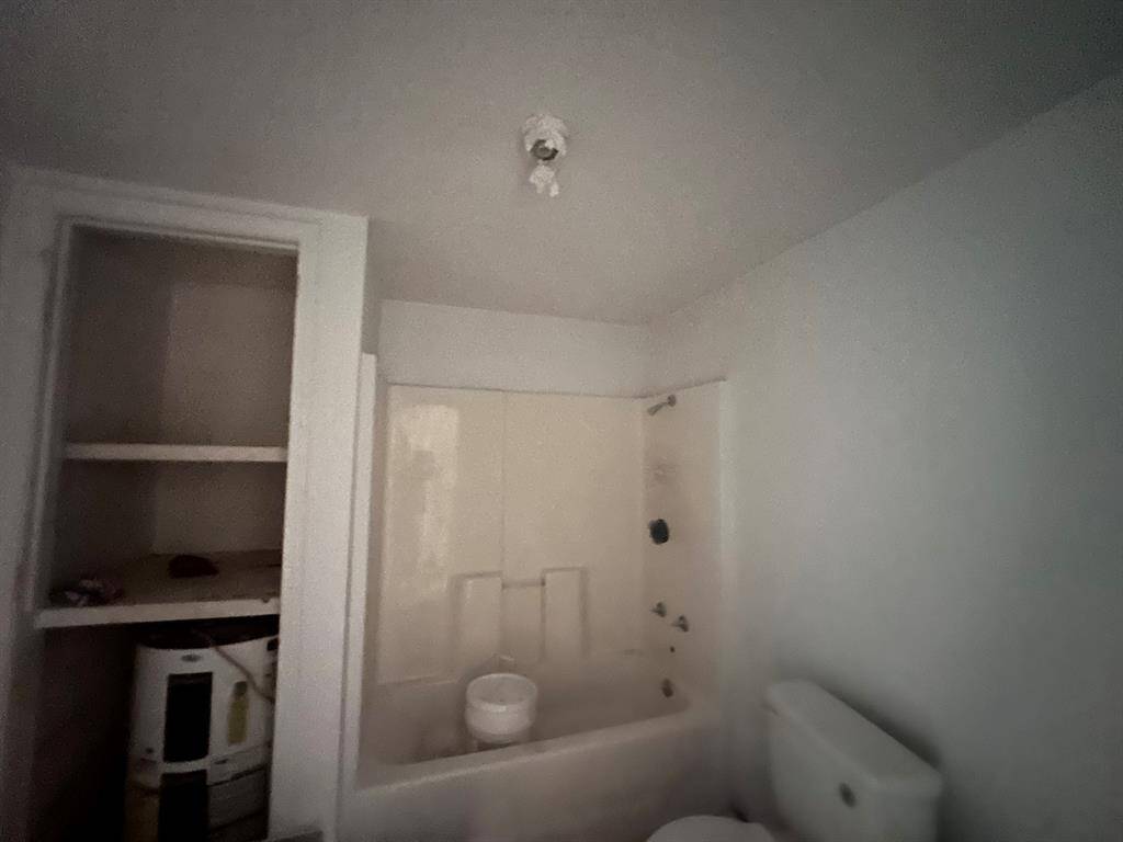 This photo shows a small bathroom with a bathtub/shower combo, a toilet, and an open shelving unit. The space appears to need some updates or repairs.