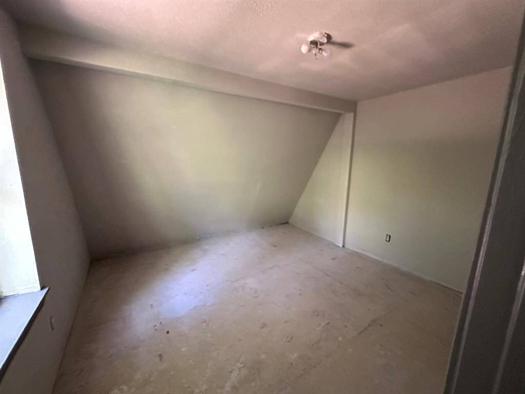 This room features a sloped ceiling and a bare floor, offering potential for customization. It has a window allowing natural light and a simple ceiling light fixture. Ideal for a small bedroom or office space.