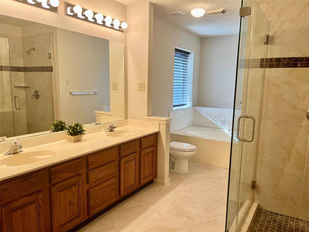 Plenty of room for two to get ready in this spacious en suite primary bathroom featuring a dual vanity, deep soaking tub, updated seamless glass walk-in shower, and a generous walk-in closet.
