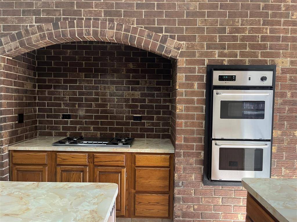 The kitchen is a standout with a stunning brick accent wall, an old-world arched alcove housing a gas cooktop, a breakfast bar, walk-in pantry, pot & pan drawers, double oven, and a second sink/wet bar area.