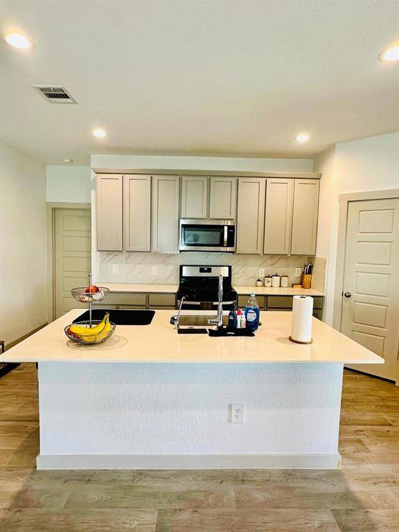 Modern kitchen with sleek light wood cabinets, a spacious island with a sink, and stainless steel appliances. The room features ample counter space, recessed lighting, and a stylish backsplash, creating a bright and inviting space for cooking and entertaining.