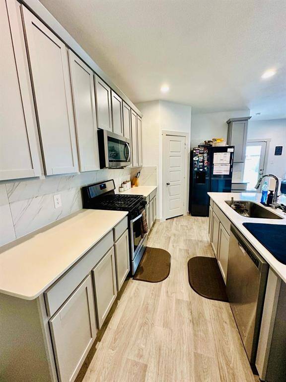 Modern kitchen with sleek light wood cabinets, a spacious island with a sink, and stainless steel appliances. The room features ample counter space, recessed lighting, and a stylish backsplash, creating a bright and inviting space for cooking and entertaining.