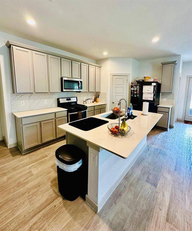 Modern kitchen with sleek light wood cabinets, a spacious island with a sink, and stainless steel appliances. The room features ample counter space, recessed lighting, and a stylish backsplash, creating a bright and inviting space for cooking and entertaining.