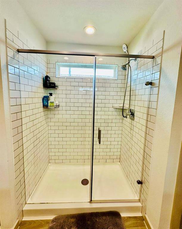 Modern walk-in shower featuring subway tile walls, a glass door, and a rain showerhead. It includes a small window for natural light and built-in shelves for toiletries.