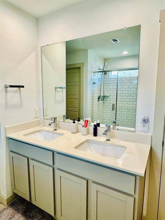 This photo shows a modern bathroom with a double vanity, large mirror, and a glass-enclosed shower with subway tile.