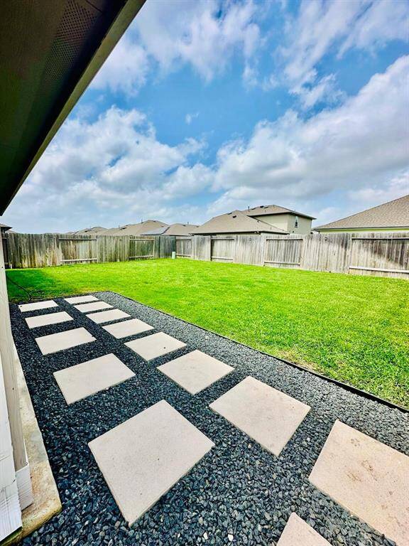 Spacious backyard featuring a well-maintained lawn, bordered by a wooden fence for privacy. A modern stone pathway adds style and functionality, perfect for outdoor activities or gatherings.