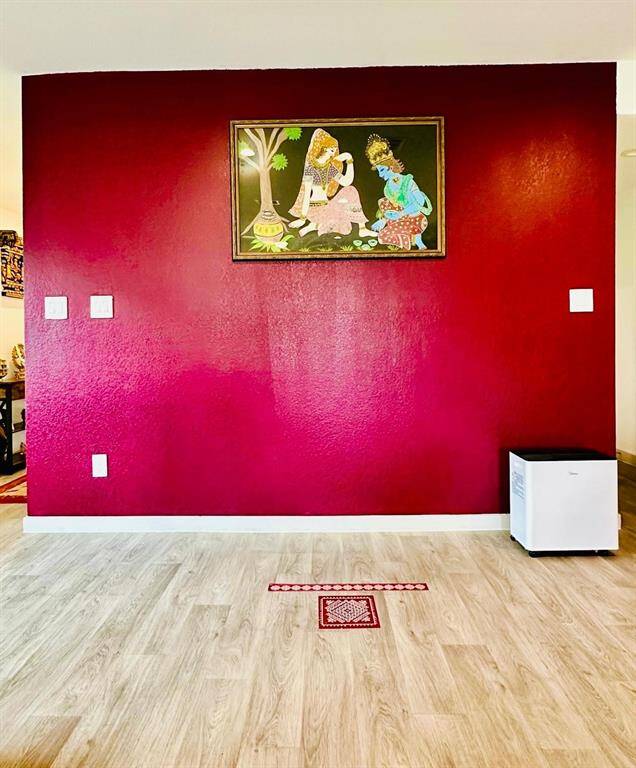 This photo shows a room with a bold maroon accent wall featuring a framed artwork. The flooring is light wood, and there's a small white appliance in the corner. The overall look is clean and modern.