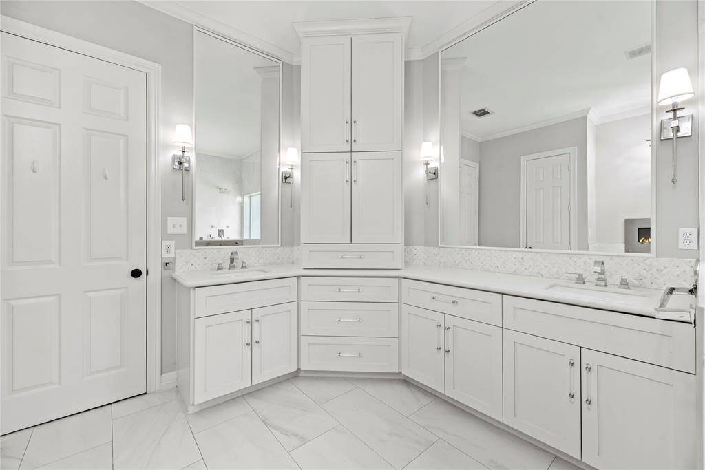 Elegantly updated primary bath with dual vanities, abundant cabinetry, and oversized mirrors, finished with beautiful white tile flooring.