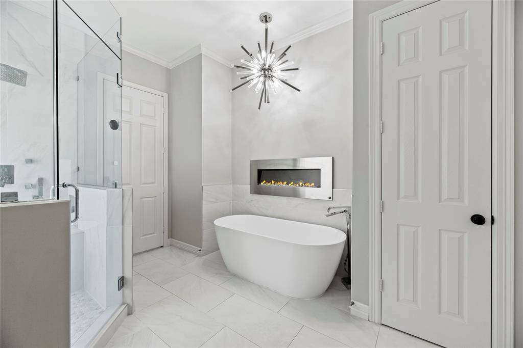 Luxurious soaking tub with a contemporary chandelier above, a cozy fireplace, and a walk-in glass shower, creating a true spa retreat.