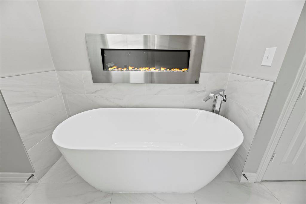 Spa-like freestanding tub set beneath a modern linear fireplace, creating a truly serene setting.