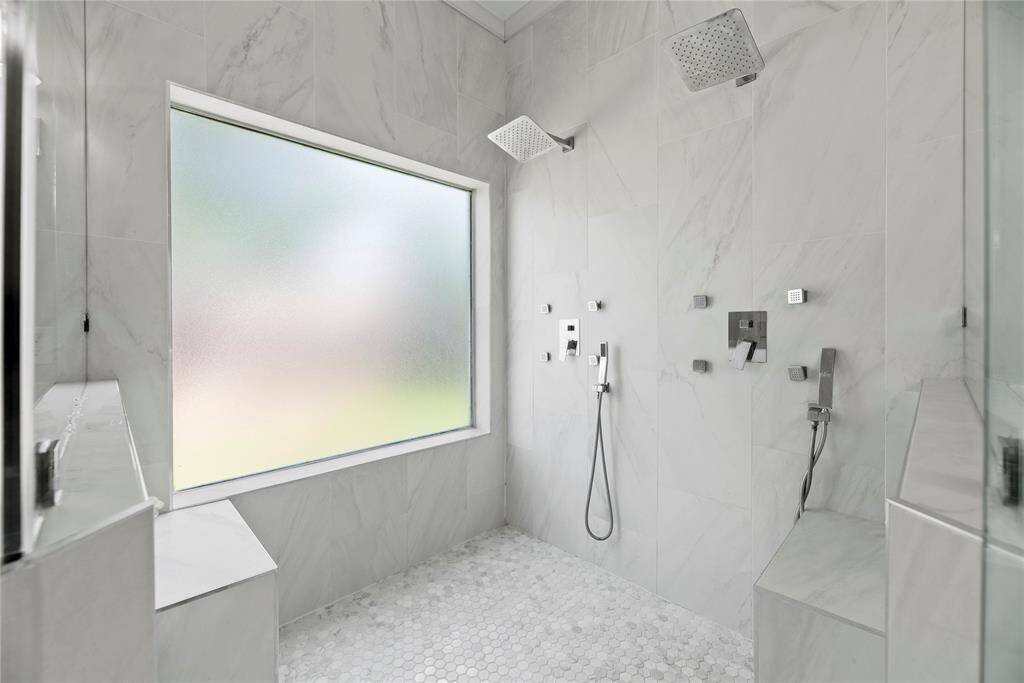 Expansive walk-in shower with dual shower heads, built-in seating, and stylish tile finishes.