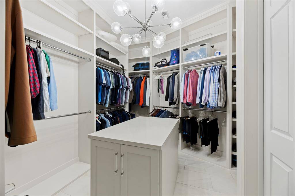 Impressive primary walk-in closet complete with custom built-ins, double hanging rods, and an island for additional storage.