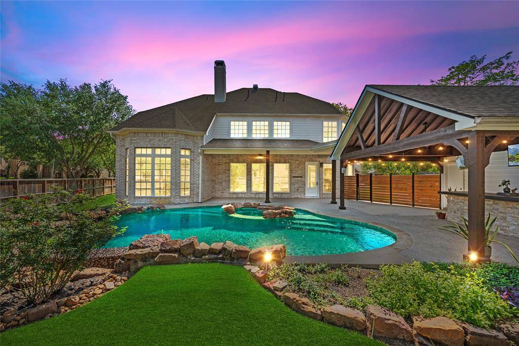 Gorgeous twilight shot of the backyard showcasing pool lighting, beautifully illuminated landscaping, and a cozy, inviting outdoor living space.