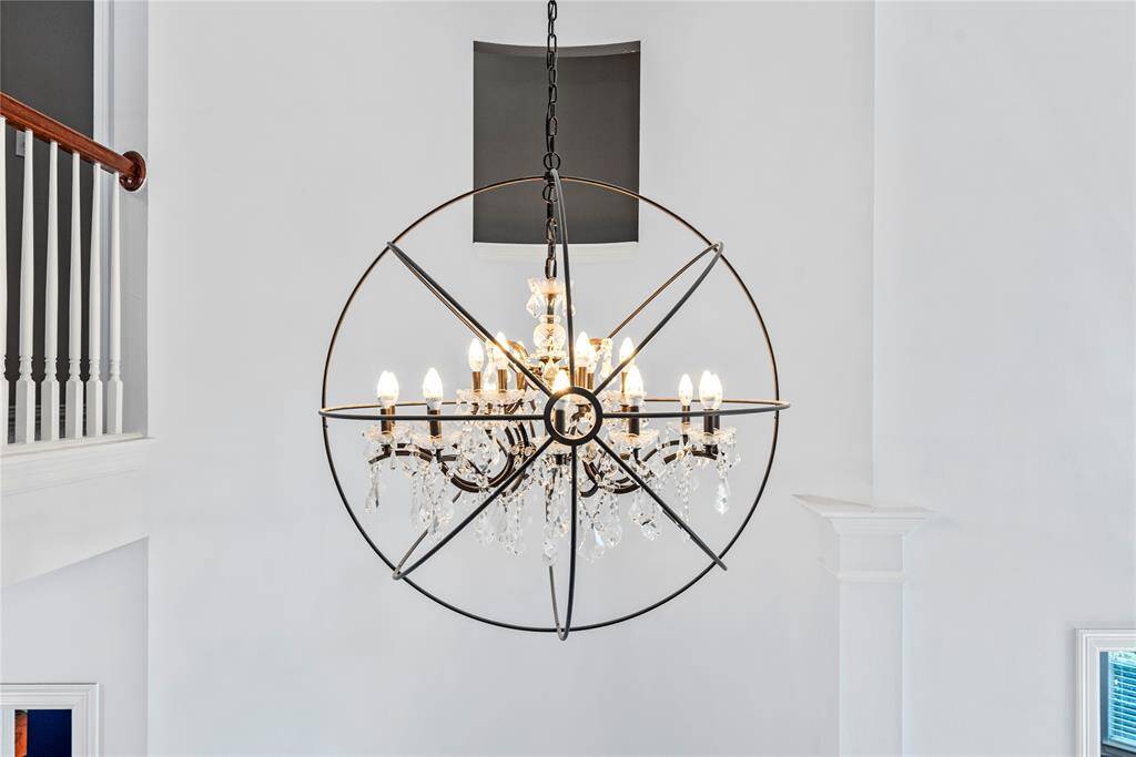 Elegant crystal chandelier framed within a dramatic spherical iron fixture, creating a stunning focal point in the grand entryway.