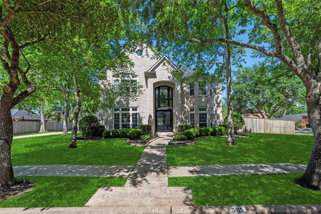 Impressive two-story brick home with a grand front entry and beautifully manicured lawn, framed by mature trees offering shade and curb appeal