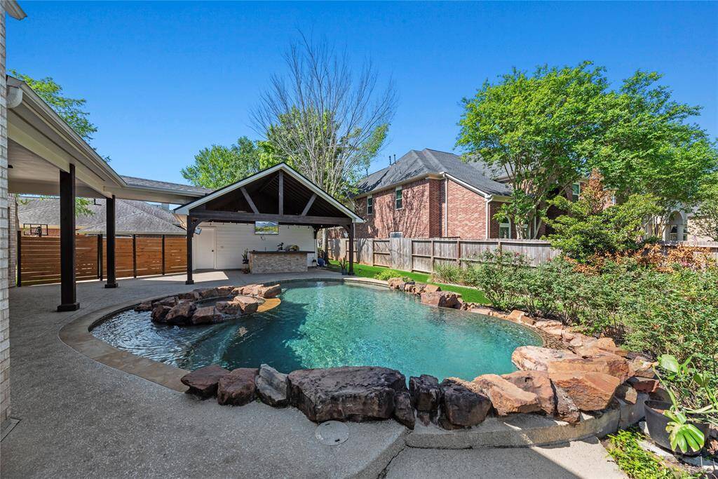 Beautiful backyard oasis featuring a heated sparkling custom-designed pool with natural stone accents, mature landscaping, and privacy fencing.
