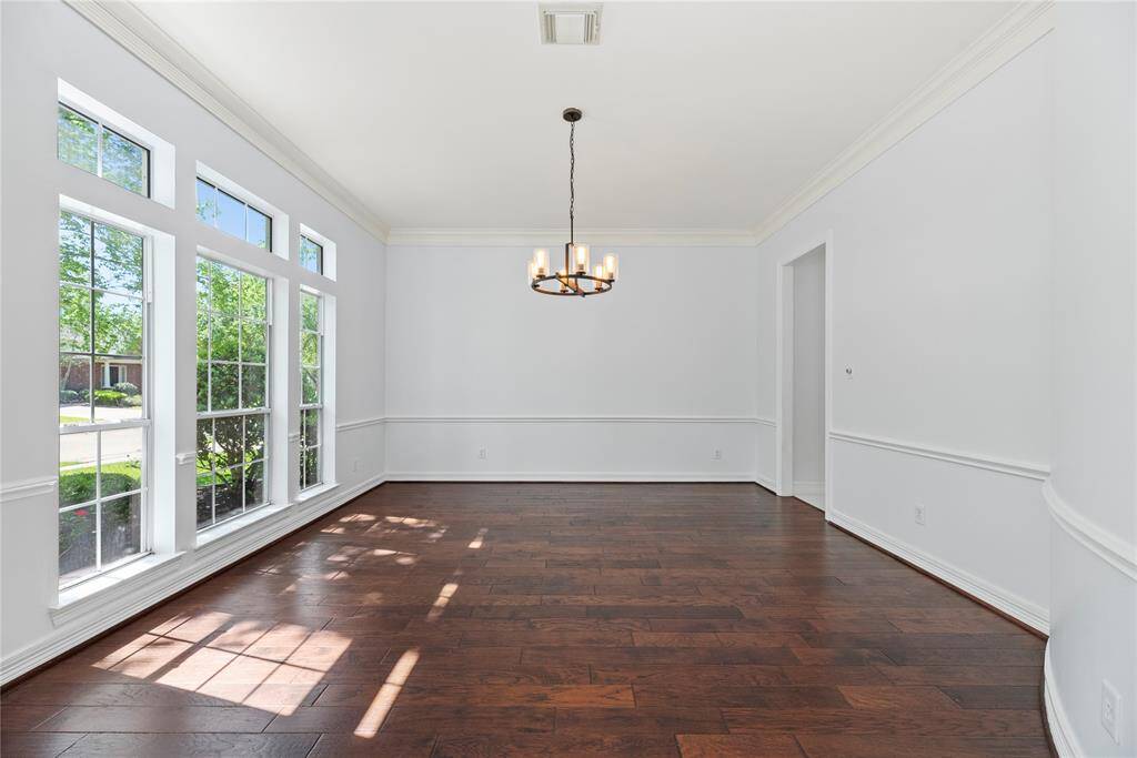 Bright and spacious formal dining room with rich hardwood floors, classic chair railing detail, and a stylish modern chandelier.