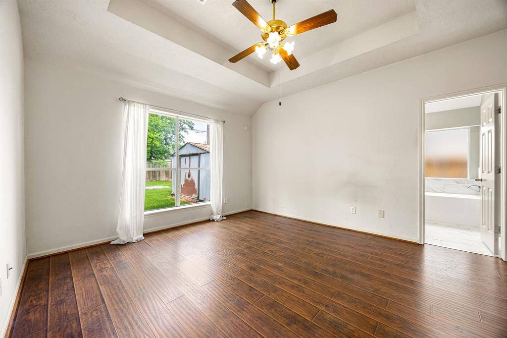 Primary bedroom has engineered hardwood flooring with in-set tray ceiling and ceiling fan.