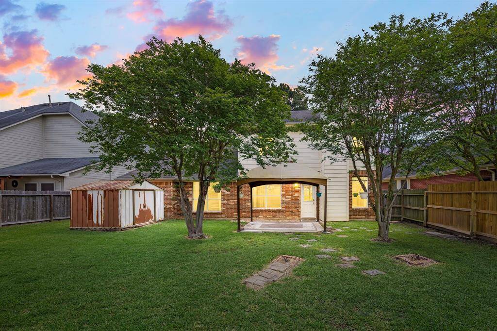 Fully fenced yard offers shade trees and a covered patio area.