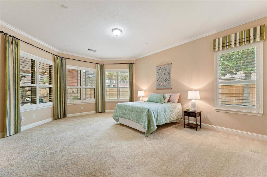 This spacious primary bedroom features large windows with 4 inch wood shutters and elegant drapery, providing plenty of natural light and a view to the outdoor oasis.