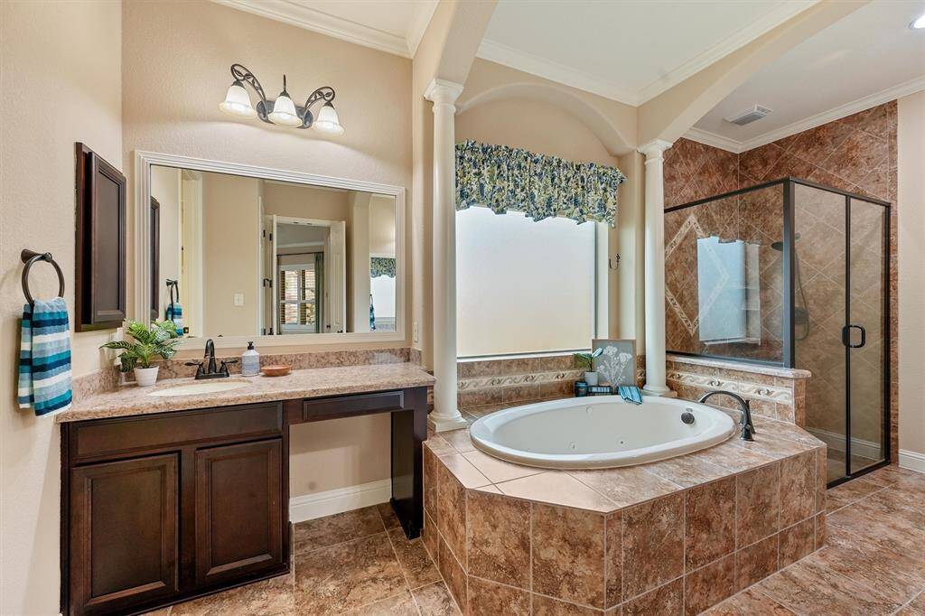 Primary bathroom features a luxurious whirlpool tub with elegant tile surround, a separate glass-enclosed shower, and a large vanity with ample counter space and storage. The room is well-lit with overhead lighting and natural light from a frosted window, creating a serene atmosphere.