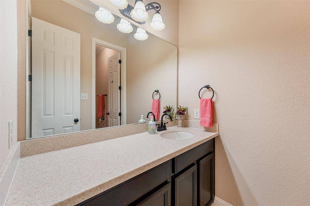 This bathroom features a spacious countertop with a single sink, large mirror, and elegant lighting. The neutral color palette is complemented by dark cabinetry offering a clean and modern look.