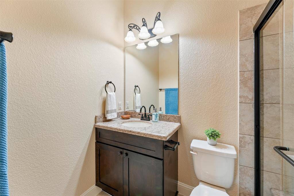 Ensuite #1 - featuring a modern sink vanity with a granite countertop and dark wood cabinetry. It has a large mirror with stylish lighting, and a glass-enclosed shower with bench seat and handrail.