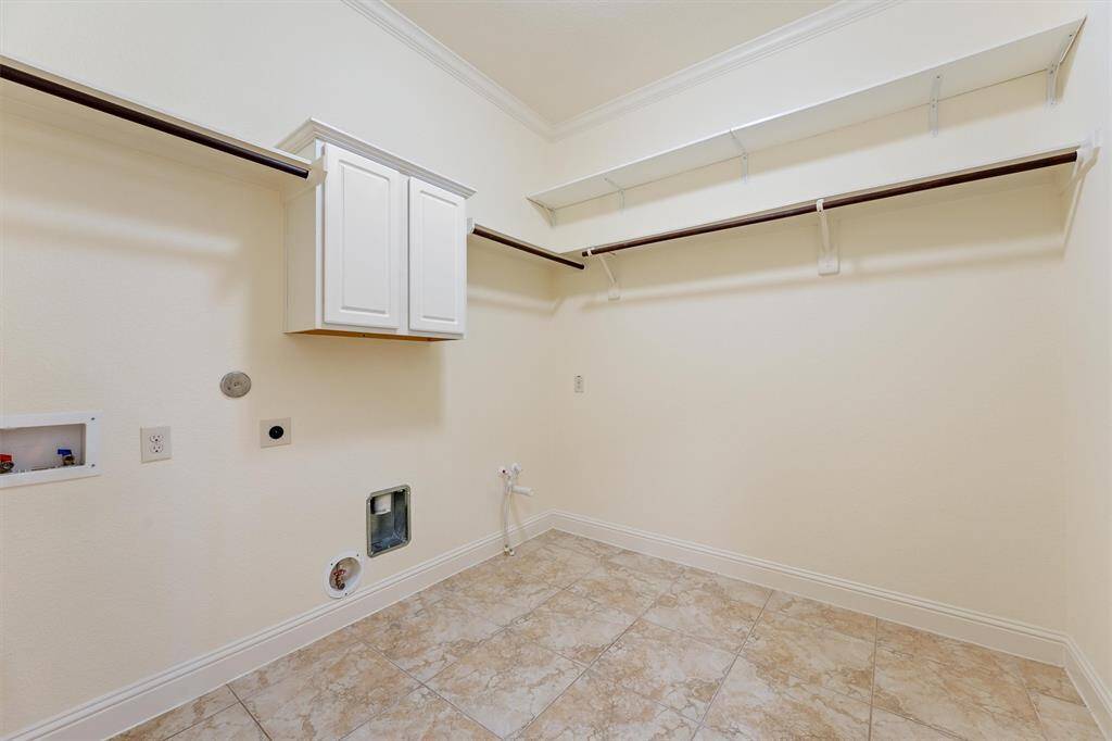 This spacious laundry room features tiled floors, hookups for a washer and dryer, a wall-mounted cabinet for storage, and ample hanging space as well as a utility sink hookup. Whole house water softner installed in garage also. Notice, even the laundry room has crown molding.
