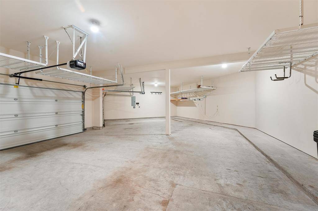 This freshly painted oversized custom 3 car garage features ample overhead storage racks, and bright lighting, perfect for parking and organizing tools or equipment.
