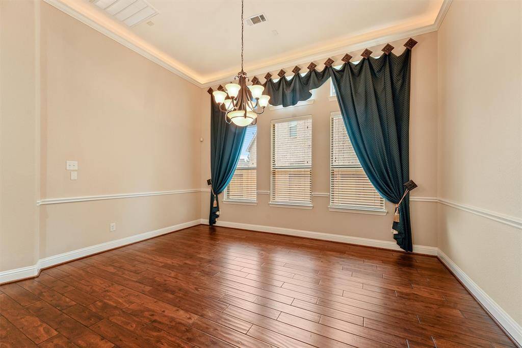 Formal dining room fit for a feast! This elegant dining room features warm hardwood floors and tall windows with custom blue drapes, complemented by crown molding and a stylish chandelier as well as accent lighting in the tray ceiling.