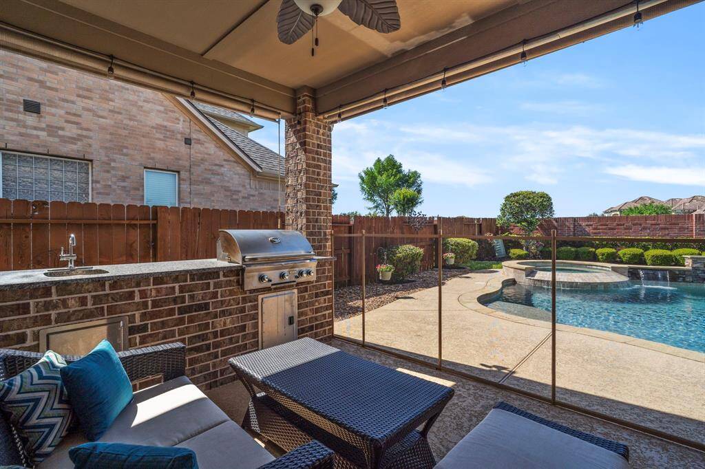The covered patio features an outdoor kitchen with stainless steel gas grill, sink, storage cabinets, and stone countertop. Cordless UV blocking exterior roller shades were installed July 2024.