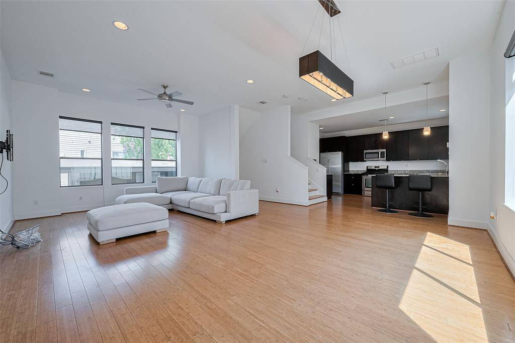 This spacious open-concept living area features hardwood flooring, abundant natural light, and a modern kitchen with stainless steel appliances and a breakfast bar. Ideal for entertaining, the room includes a ceiling fan, recessed lighting, and a cozy sectional sofa.