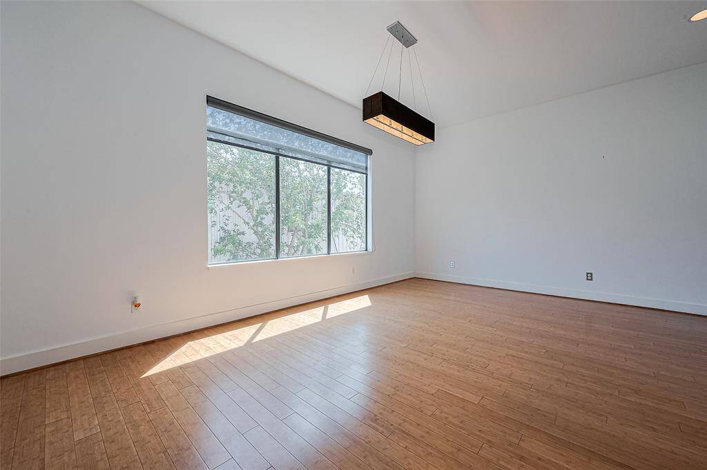 This spacious room features a large window with abundant natural light, bamboo flooring, and a modern rectangular pendant light, creating a bright and inviting atmosphere.