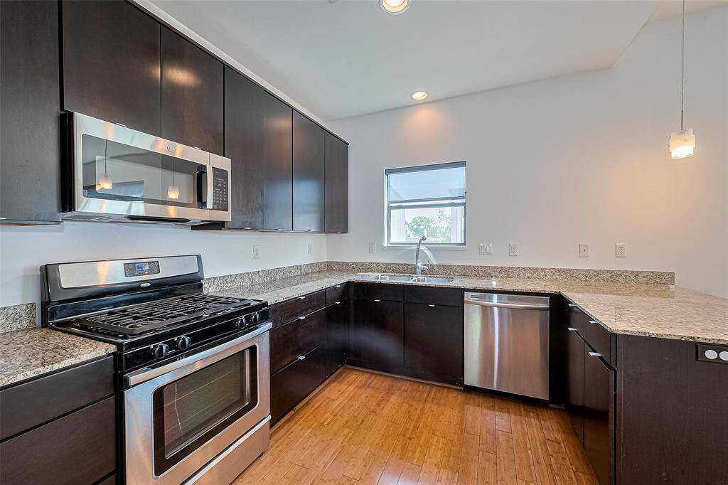 Modern kitchen with dark wood cabinets, granite countertops, and stainless steel appliances, including a gas stove and dishwasher. It features a window for natural light and sleek, minimalist design.