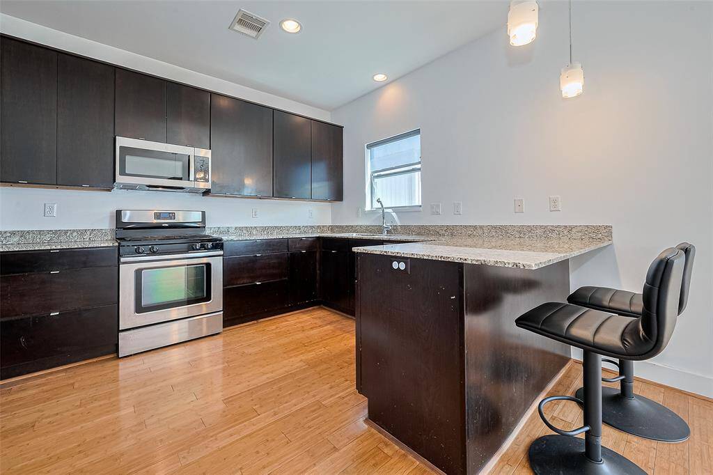 This modern kitchen features sleek dark cabinetry, stainless steel appliances, and granite countertops. It offers ample counter space and includes a breakfast bar with stylish seating, perfect for casual dining. The room is well-lit with recessed and pendant lighting, enhancing its contemporary appeal.