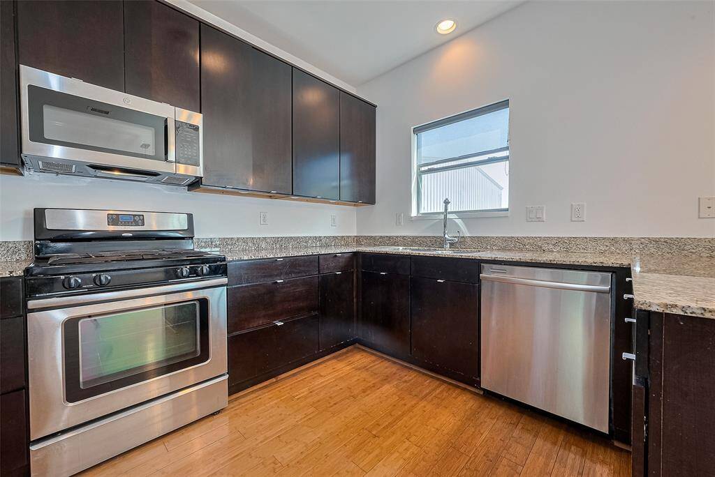Modern kitchen with stainless steel appliances, dark wood cabinets, and granite countertops. Features include a gas stove, microwave, dishwasher, and a window above the sink for natural light.