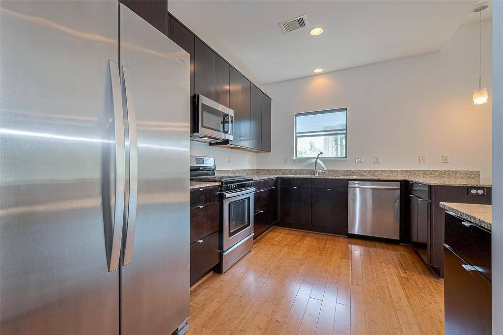 This modern kitchen features sleek stainless steel appliances, dark cabinetry, granite countertops, and bamboo flooring, offering a stylish and functional space for cooking and entertaining.