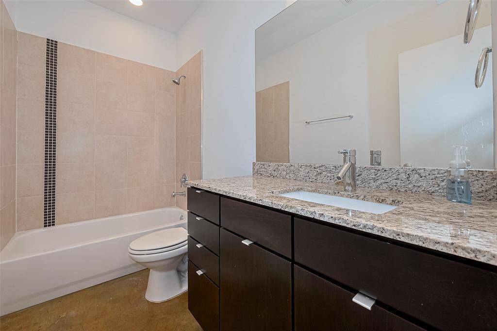 This modern bathroom features a sleek design with a granite countertop, dark cabinetry, and a tiled shower-bath combo. The neutral tones and large mirror enhance the sense of space and light.