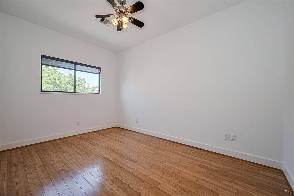 This photo showcases a bright, unfurnished room with light wood flooring and a ceiling fan. A window allows natural light and a view of greenery outside, creating an inviting atmosphere.