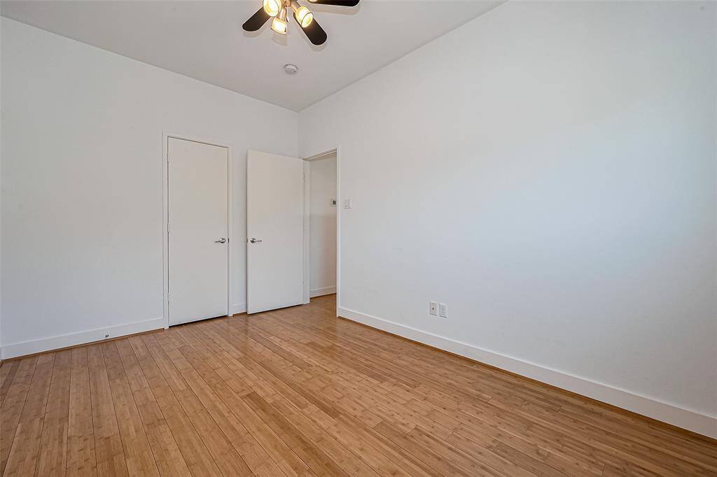 This room features clean white walls, natural wood flooring, and a ceiling fan with lights. It has two doors, offering functional access and storage options.