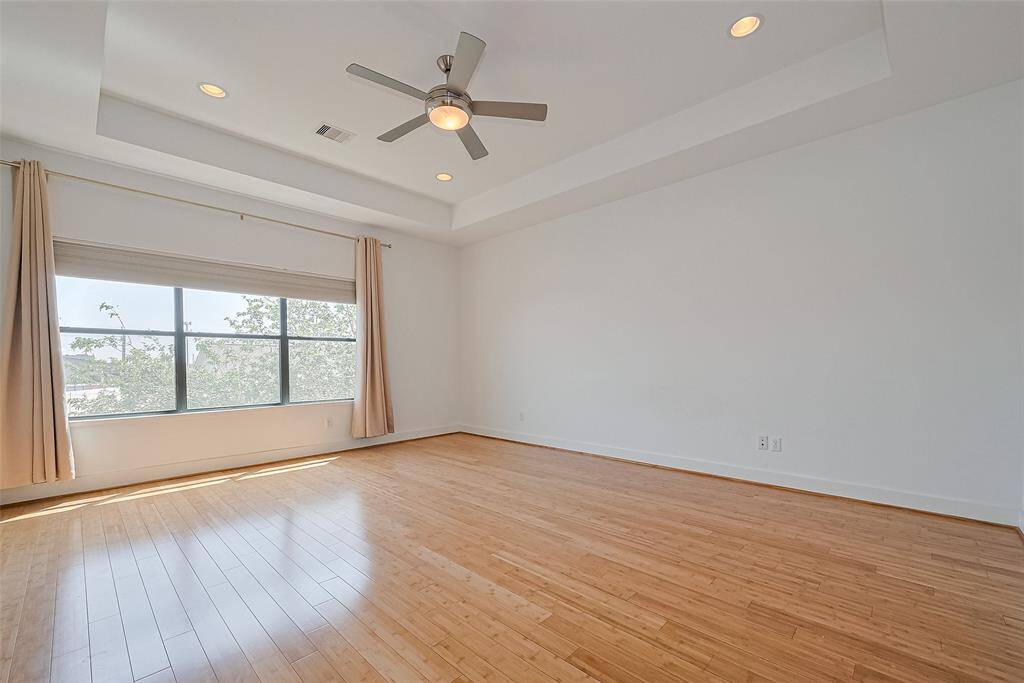 This spacious room features hardwood floors, a large window with ample natural light, and a ceiling fan, creating a bright and airy atmosphere.