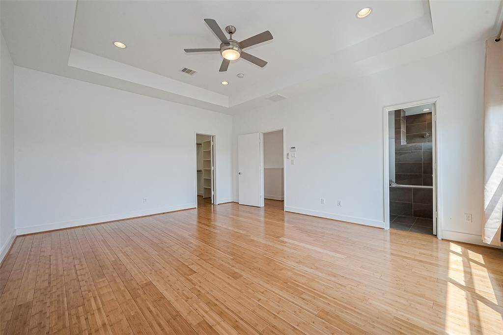 This bright room features hardwood floors, a ceiling fan, and recessed lighting. It includes a walk-in closet and an en-suite bathroom with modern tile work.