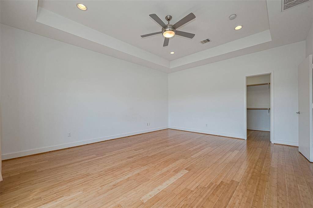 This spacious bedroom features hardwood floors, recessed lighting, a ceiling fan, and a walk-in closet, offering a modern and inviting atmosphere.