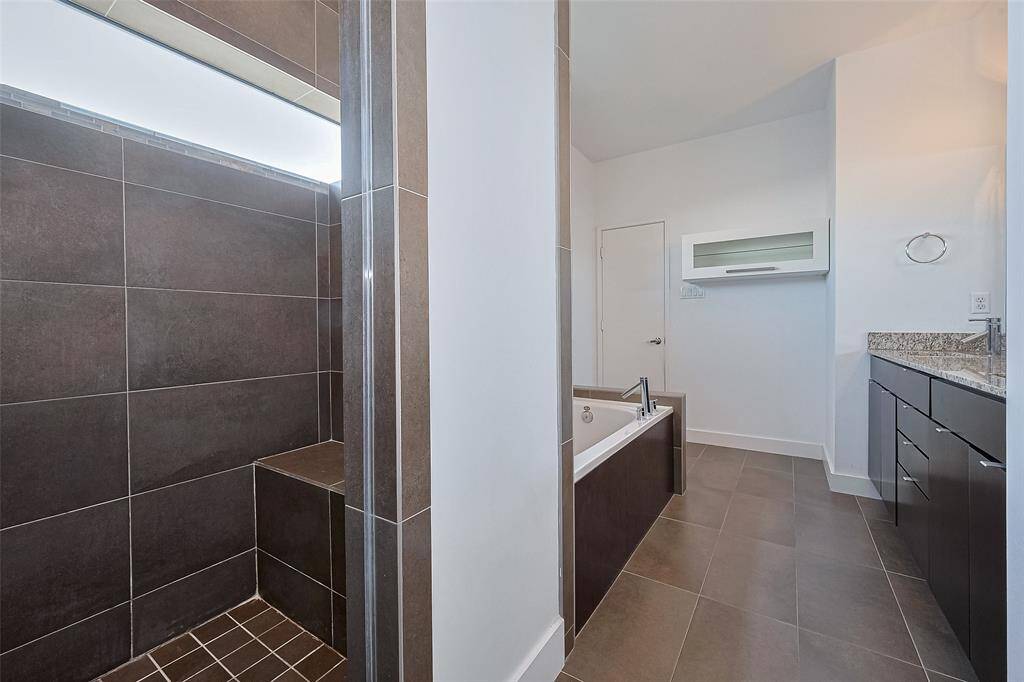 Modern bathroom featuring a spacious walk-in shower with dark tiles, a sleek bathtub, and a granite countertop vanity. Bright and clean design with ample space for comfort.