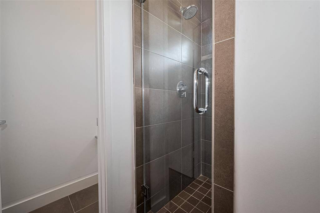 This photo features a modern shower with a glass door and chrome handle, set against large, neutral-toned tiles for a sleek and clean look.