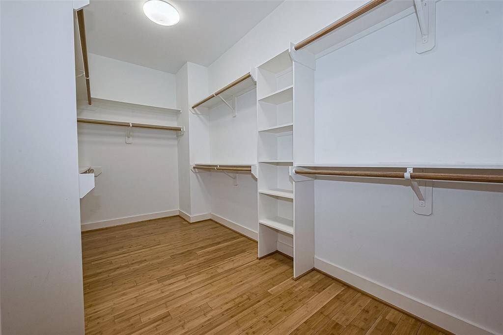 Spacious walk-in closet with wooden flooring, ample hanging space, and built-in shelving for organized storage. Bright and well-lit for convenience.